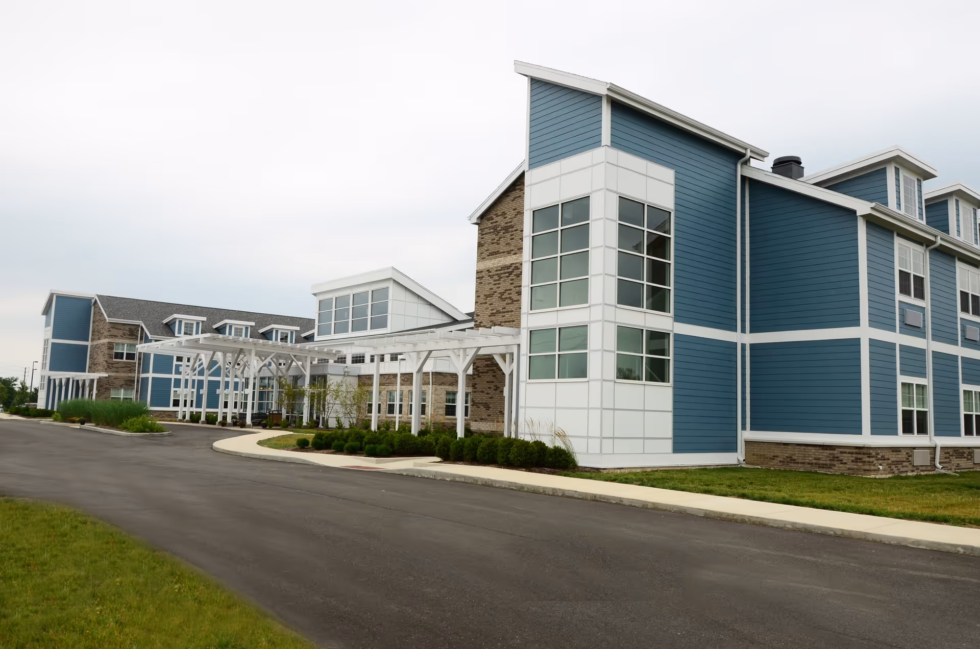 Modern blue-and-white senior living facility building with a covered entrance and paved driveway.