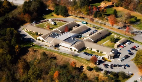 Aerial view of Princeton Health Care Center's single-story building complex with parking lots surrounded by trees in autumn.