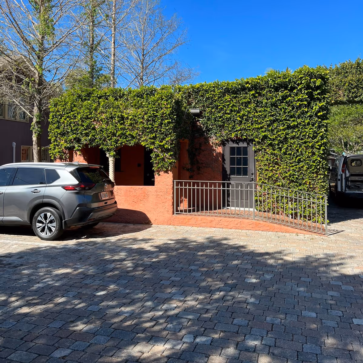 Entrance to ivy-covered orange brick building with a railing and parked cars.
