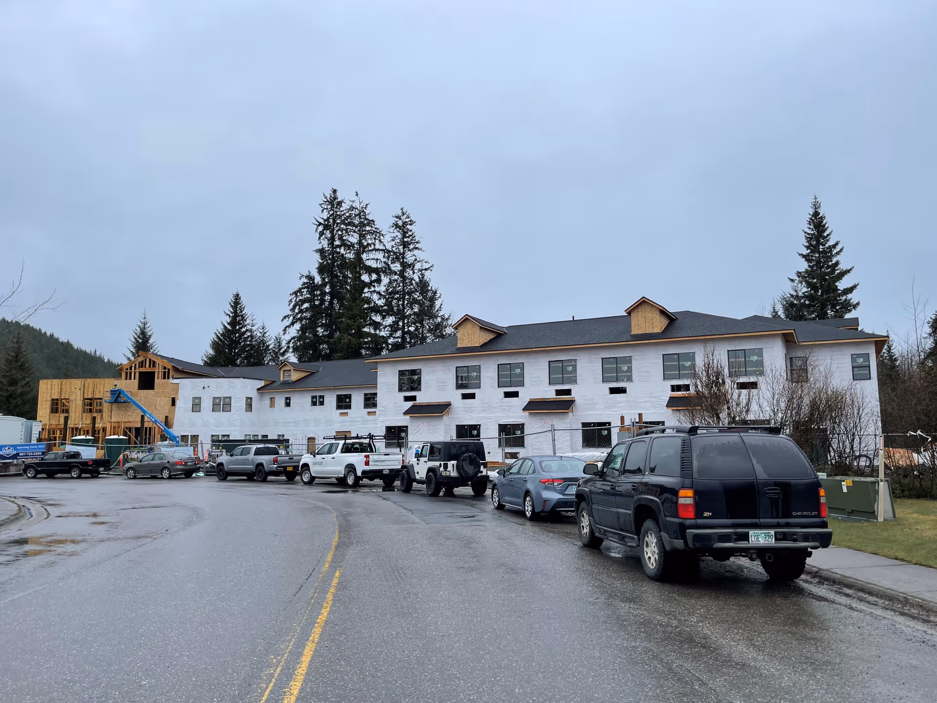Exterior front of Riverview Senior Living under construction with parked cars along a wet road.