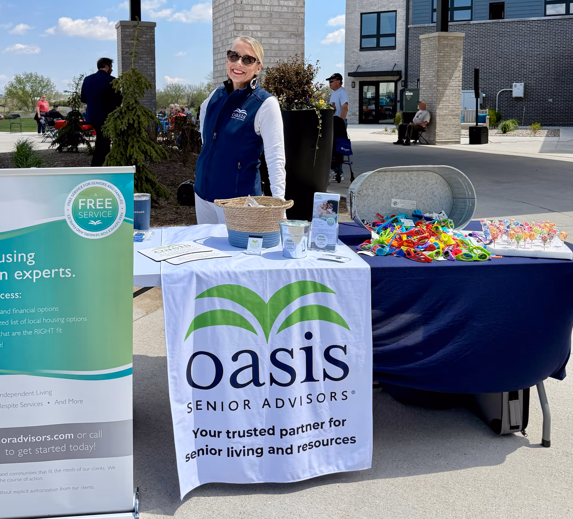Outdoor promotional table for Oasis Senior Advisors Lincoln with a staff member smiling beside banners.