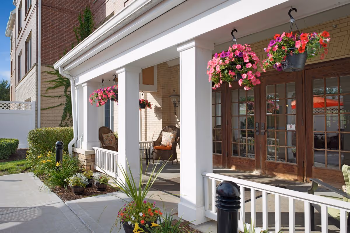Front entrance porch with hanging flower baskets, wicker chairs, and glass double doors.