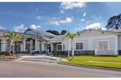 Front view of a single-story Mease Life facility with light blue exterior, palm trees, and lawn.