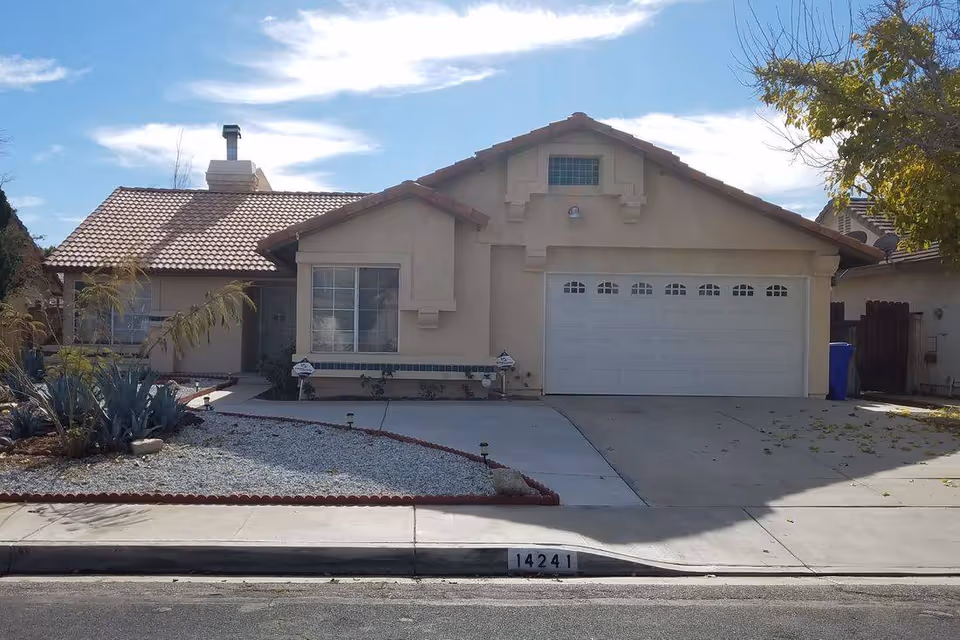 Front exterior view of a single-story house with a tiled roof, a two-car garage, a driveway, and a front yard landscaped with gravel and plants. The house number 14241 is visible on the curb.