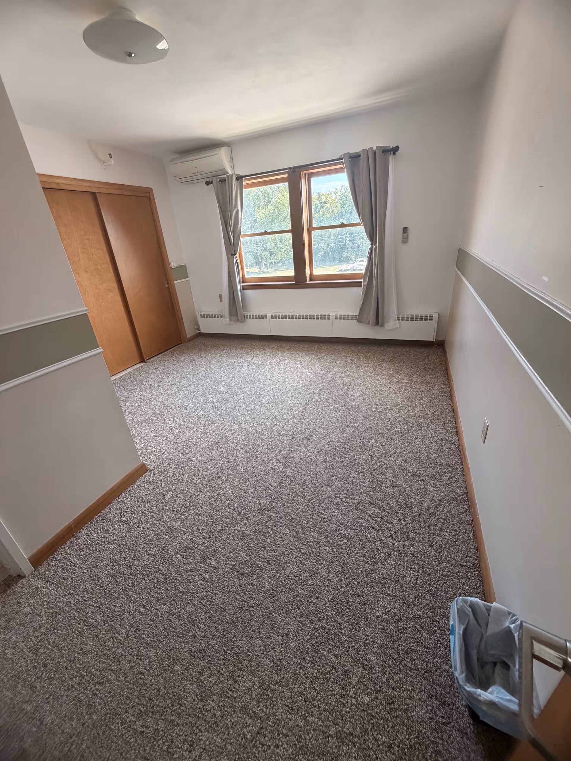 Empty bedroom with window, curtains, closet doors, and carpet in Brown Wilcox Retirement Home.