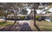 Exterior view of a single-story senior living facility, Kiva at Canterbury, with trees and a driveway.