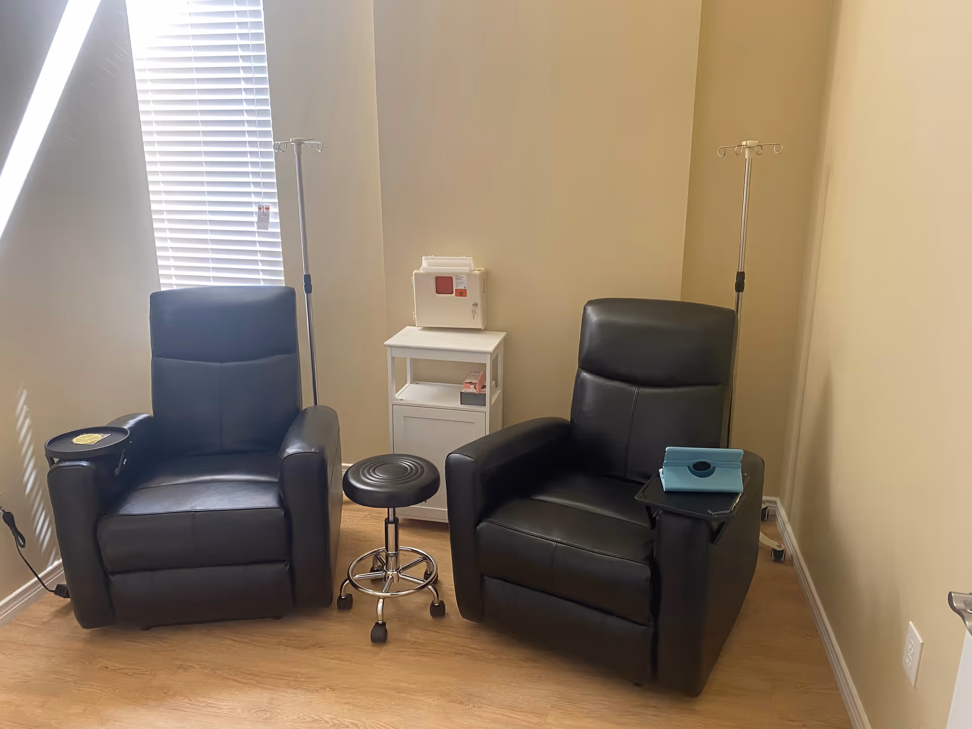 Two black leather chairs, IV stands, and a small cabinet in a treatment room.