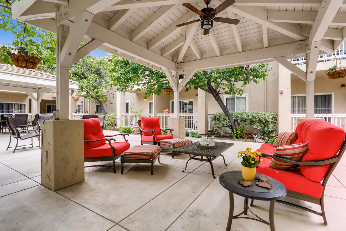 Shaded outdoor lounge with red-cushioned seating, tables, and hanging planters.