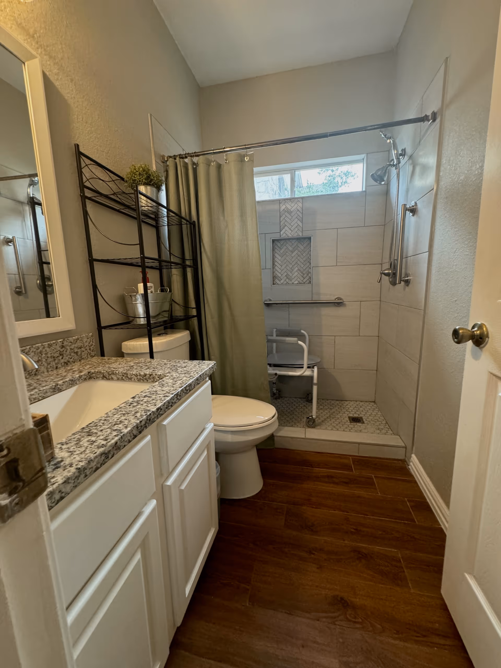 Accessible bathroom with granite countertop, white cabinets, toilet, shower, and a shower chair.