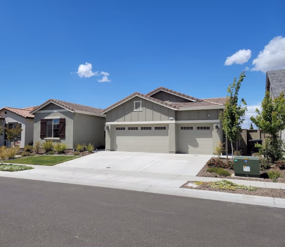 Front exterior of a suburban house with three-car garage and neatly landscaped yard.