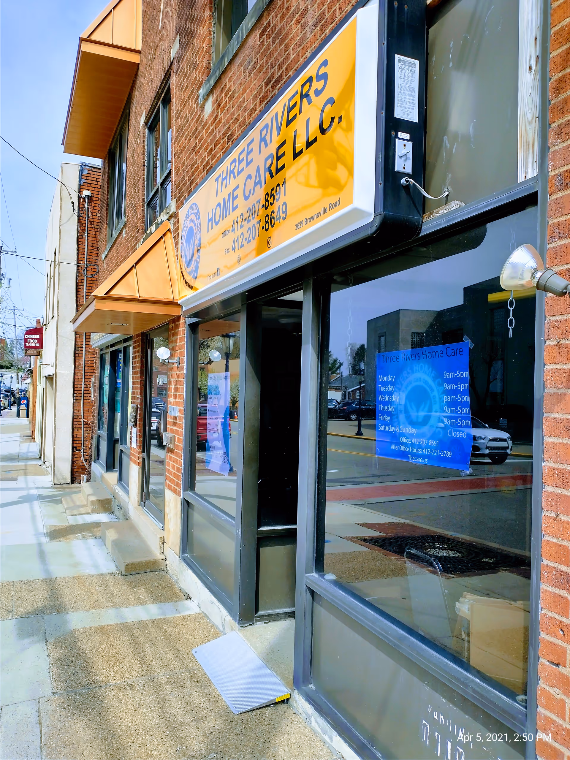 Exterior brick storefront with a yellow Three Rivers Home Care sign along the sidewalk