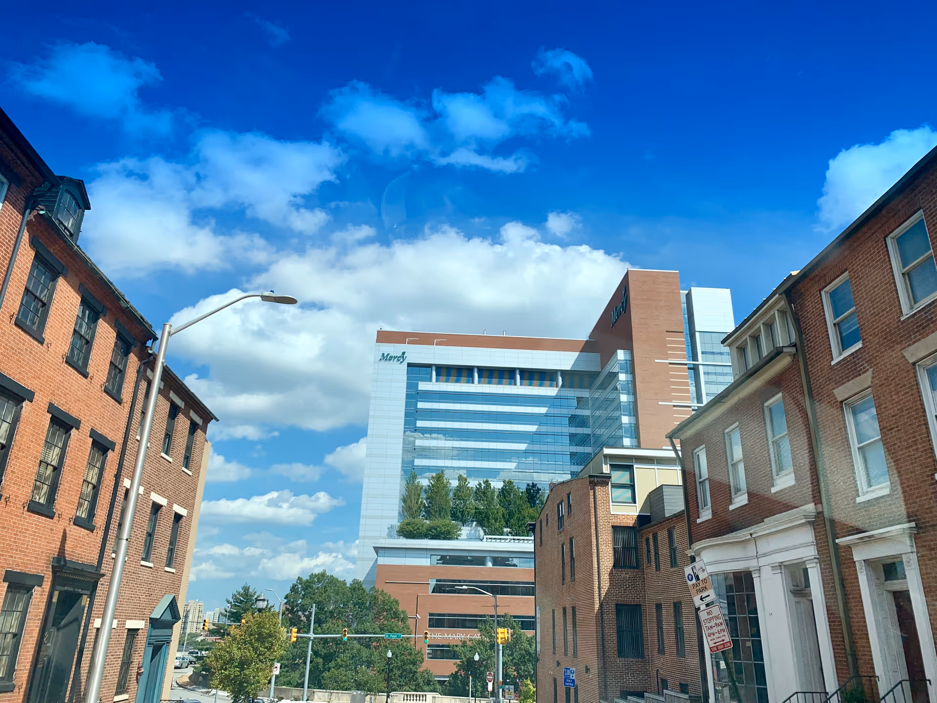 Street view of Mercy Medical Center's modern glass building behind brick rowhouses under blue sky