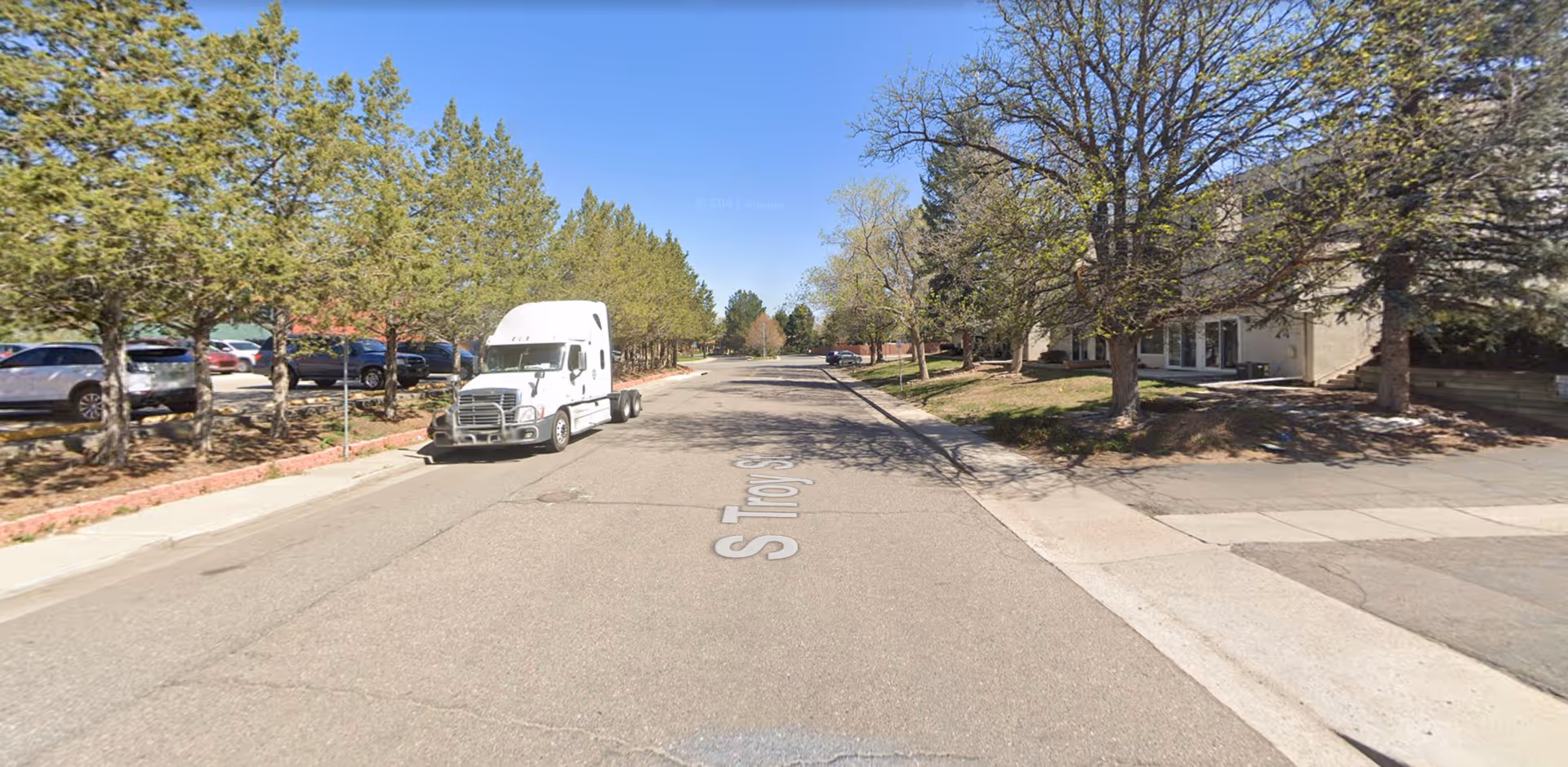Wide street scene outside a senior care facility, with a white truck and parked cars.