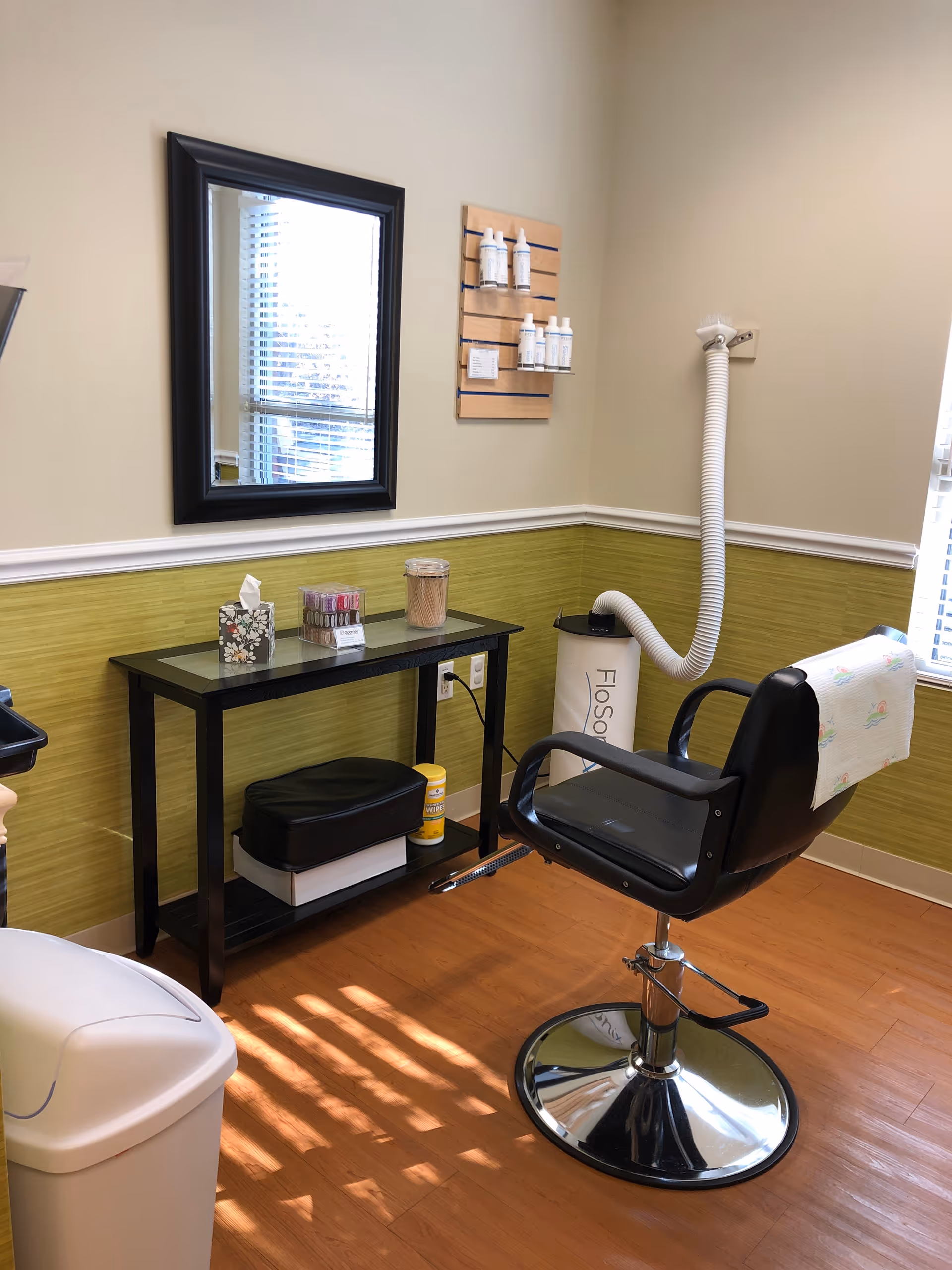 Hair styling chair and station with mirror, products, and supplies in a pastel-walled treatment room.