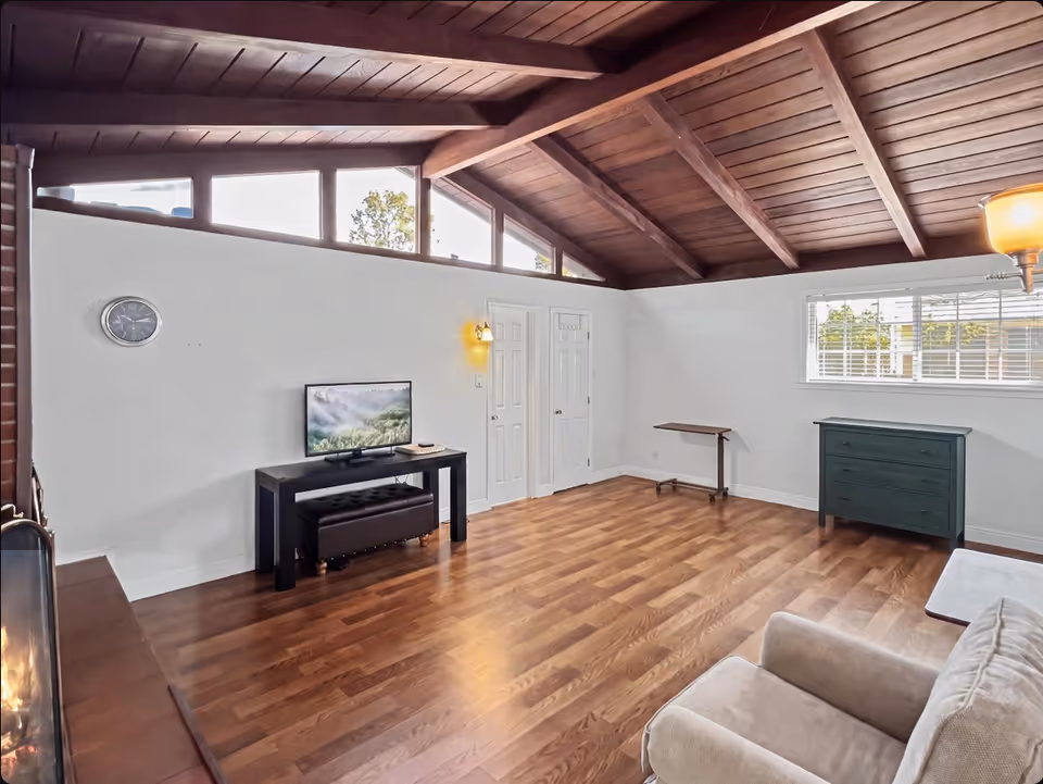 Spacious living room with vaulted wood ceiling, TV, sofa, dresser, and window blinds.