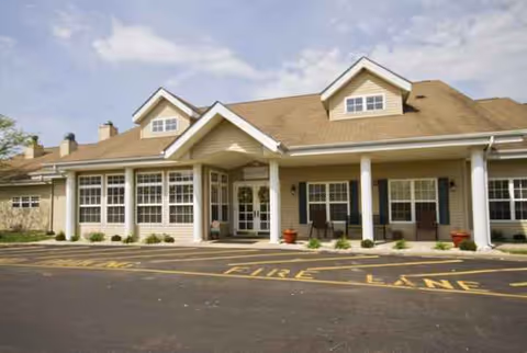 Front view of Whitlock Place senior living facility with entrance, pillars, and parked cars.