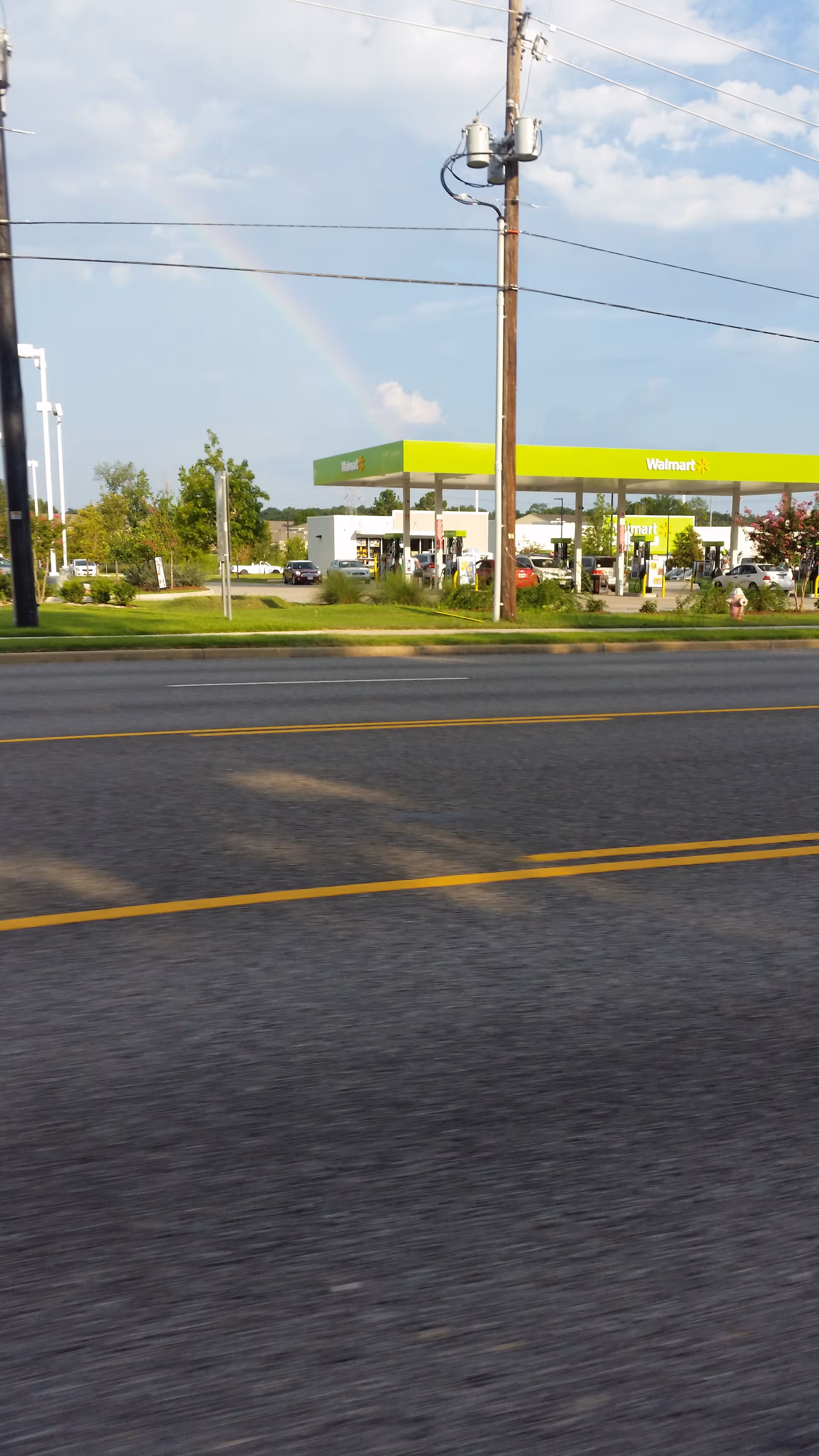 Front view of a Walmart with a bright green canopy and gas pumps, across a road.