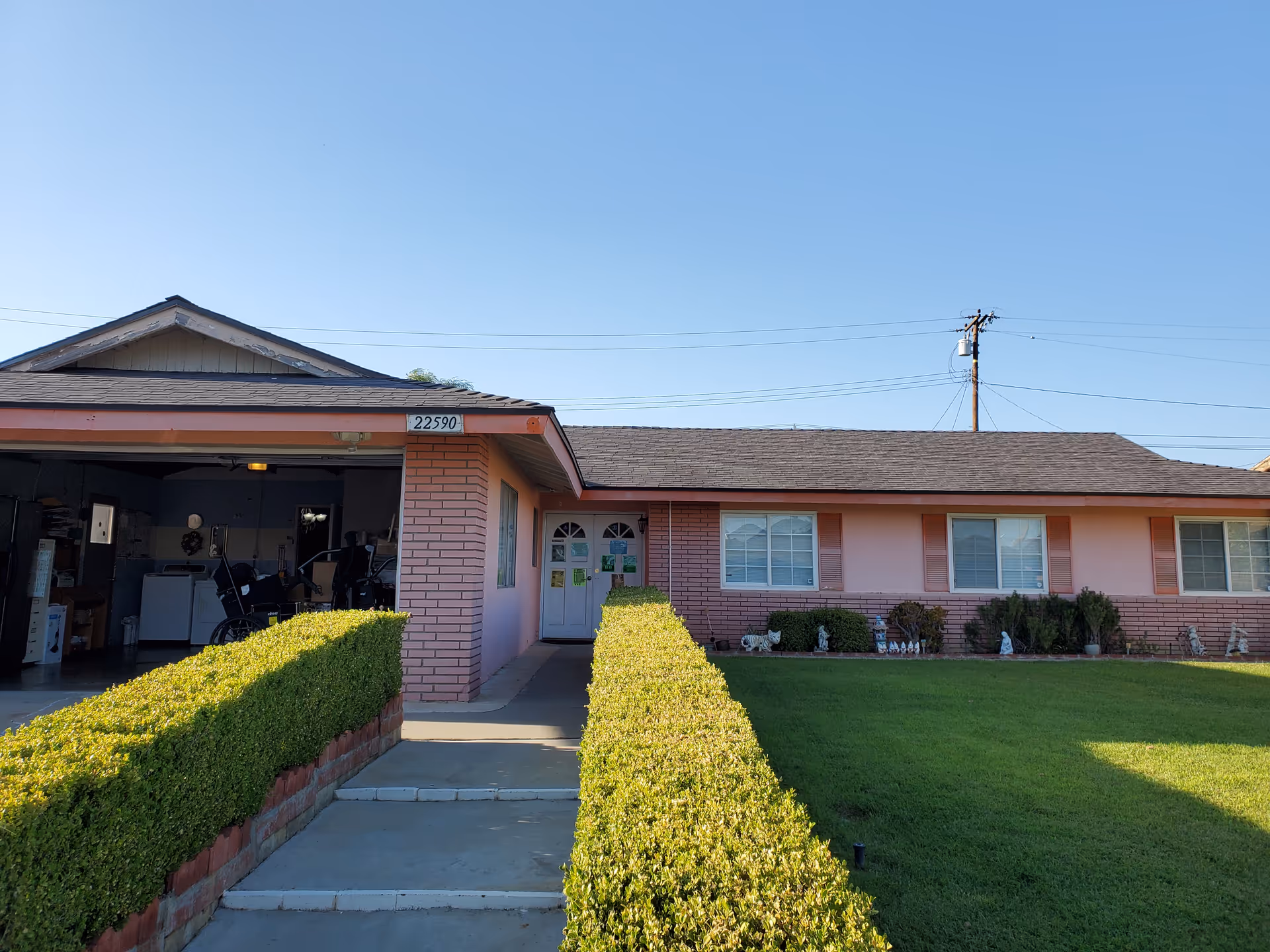 A single-story pink brick senior living facility with a manicured hedge and front entrance.