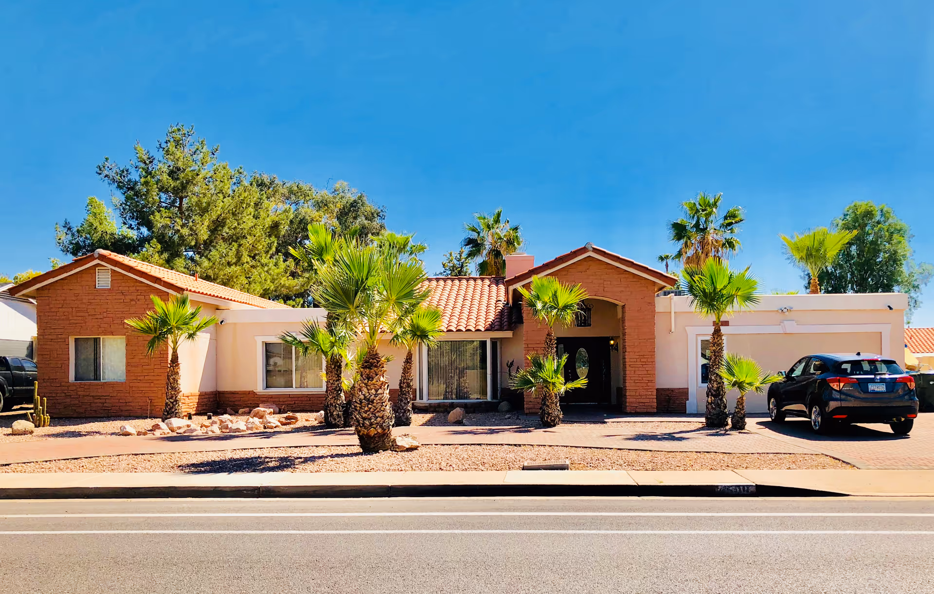 Single-story light-pink facility with stone accents, palm trees, and a parked car in front.