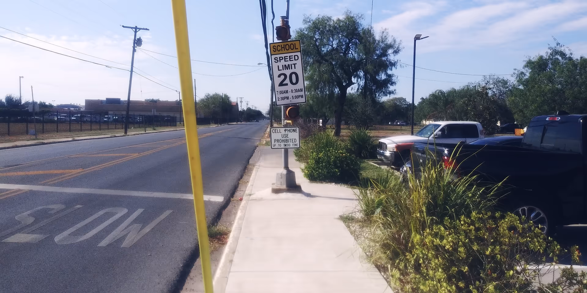 Street view with sidewalk, speed limit sign, and parked cars along the road.