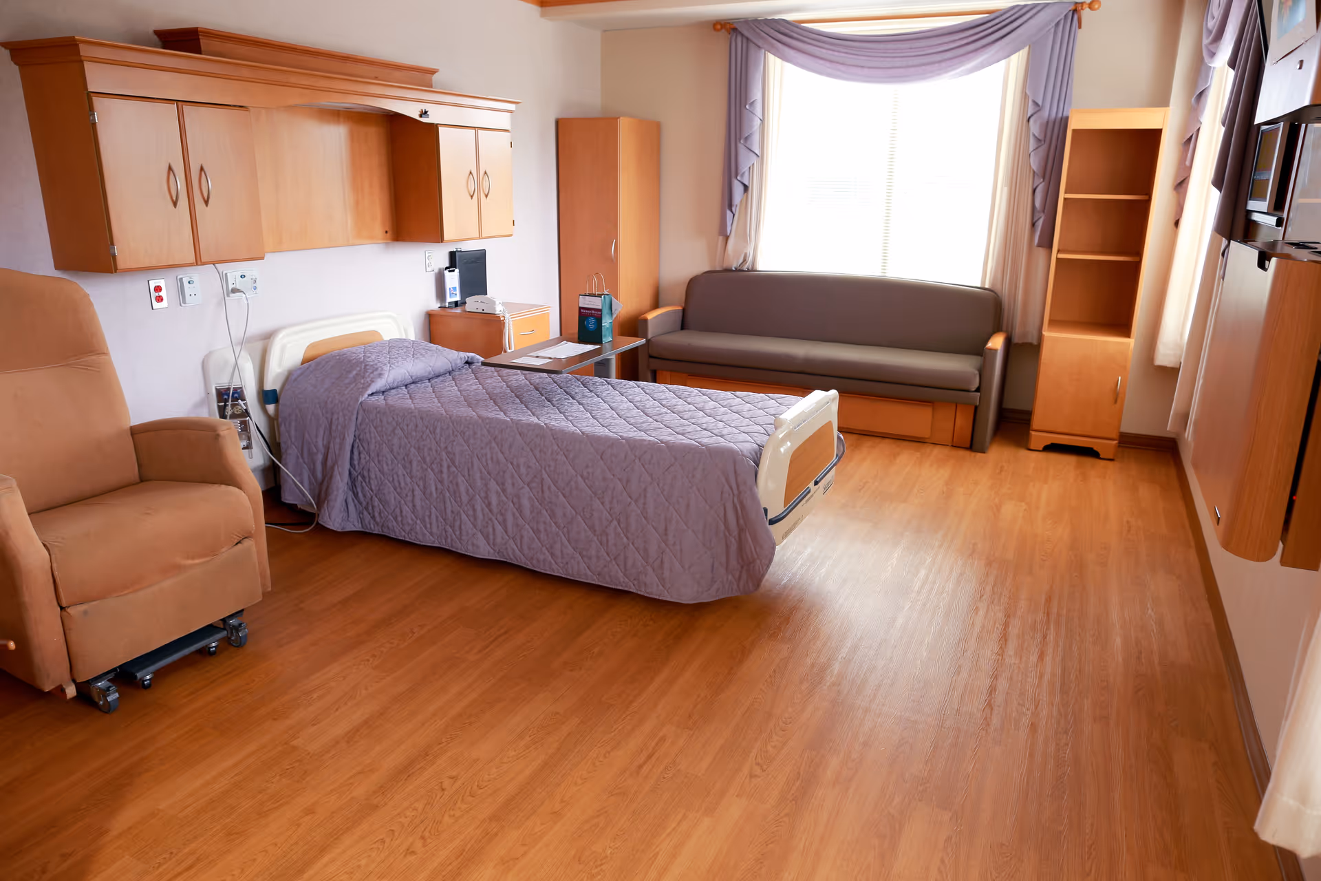 A furnished senior living bedroom with bed, sofa, cabinet, and large window.