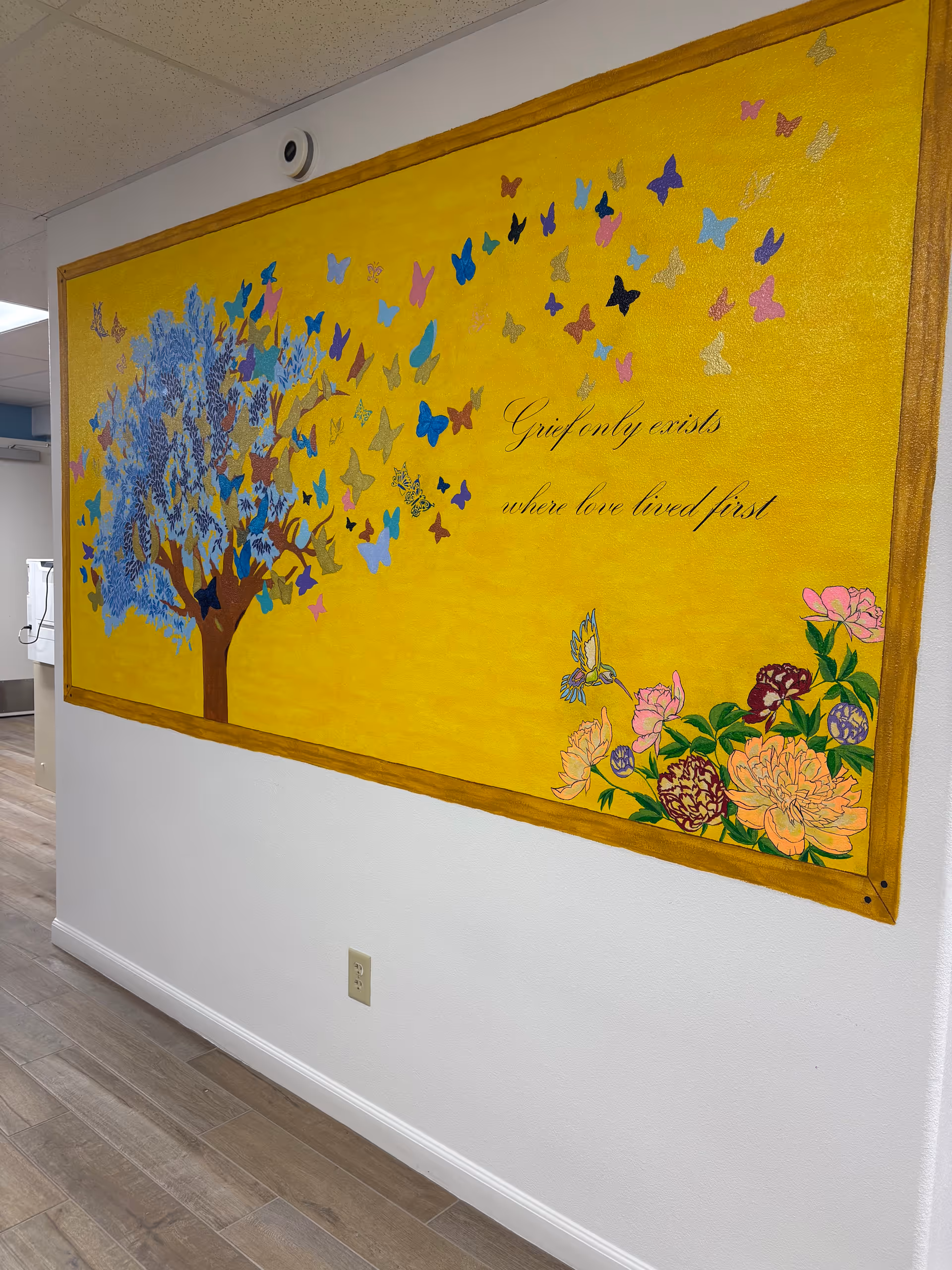 Yellow mural of a butterfly-filled tree and flowers on an interior hallway.