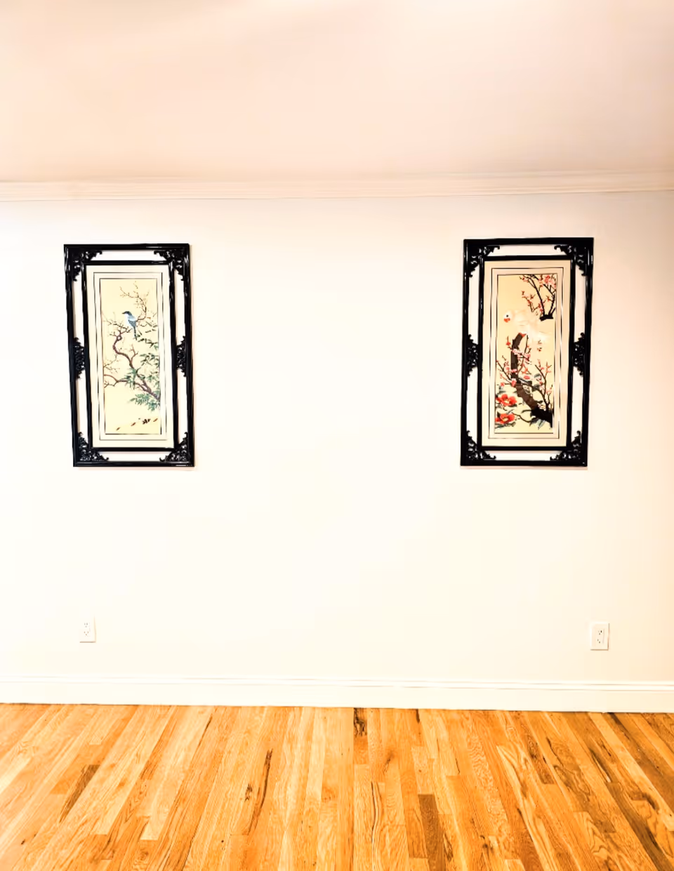 Two framed pictures hang on a white wall above a wooden floor.