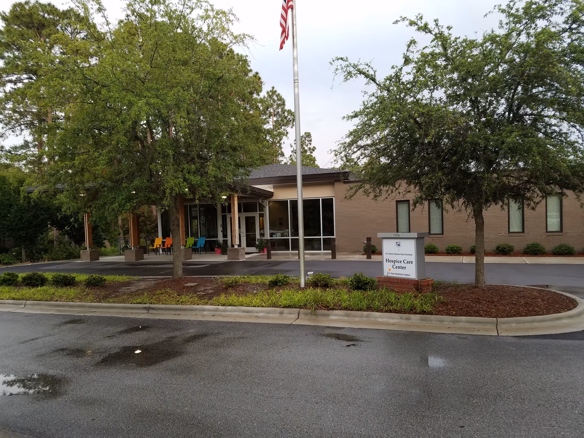 Exterior view of a Lower Cape Fear LifeCare facility entrance with trees and a flagpole.