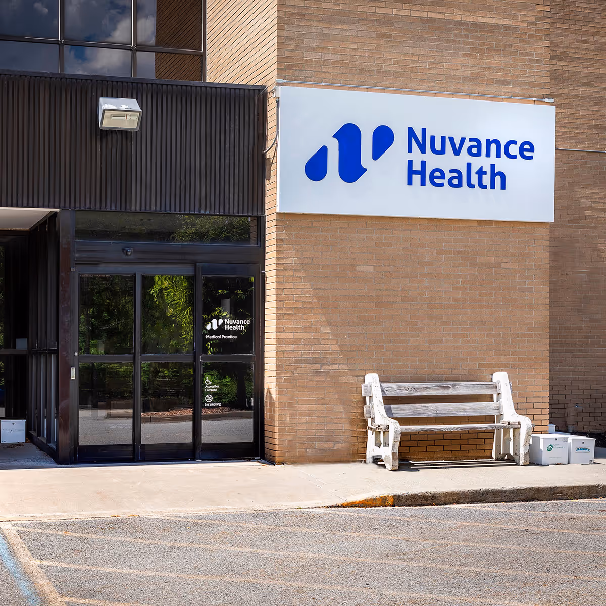 Exterior brick building with a large Nuvance Health sign, glass doors, and a bench.