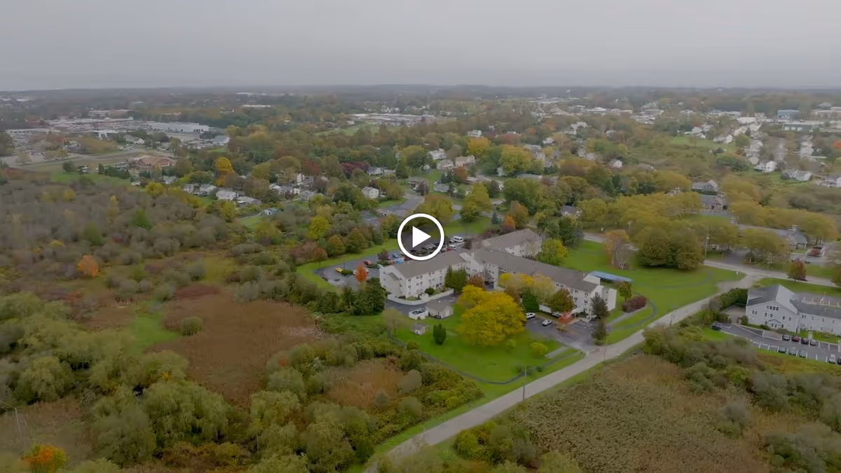 Aerial view of a senior living facility named Blenheim-Newport surrounded by trees and greenery with a residential neighborhood in the background under an overcast sky.