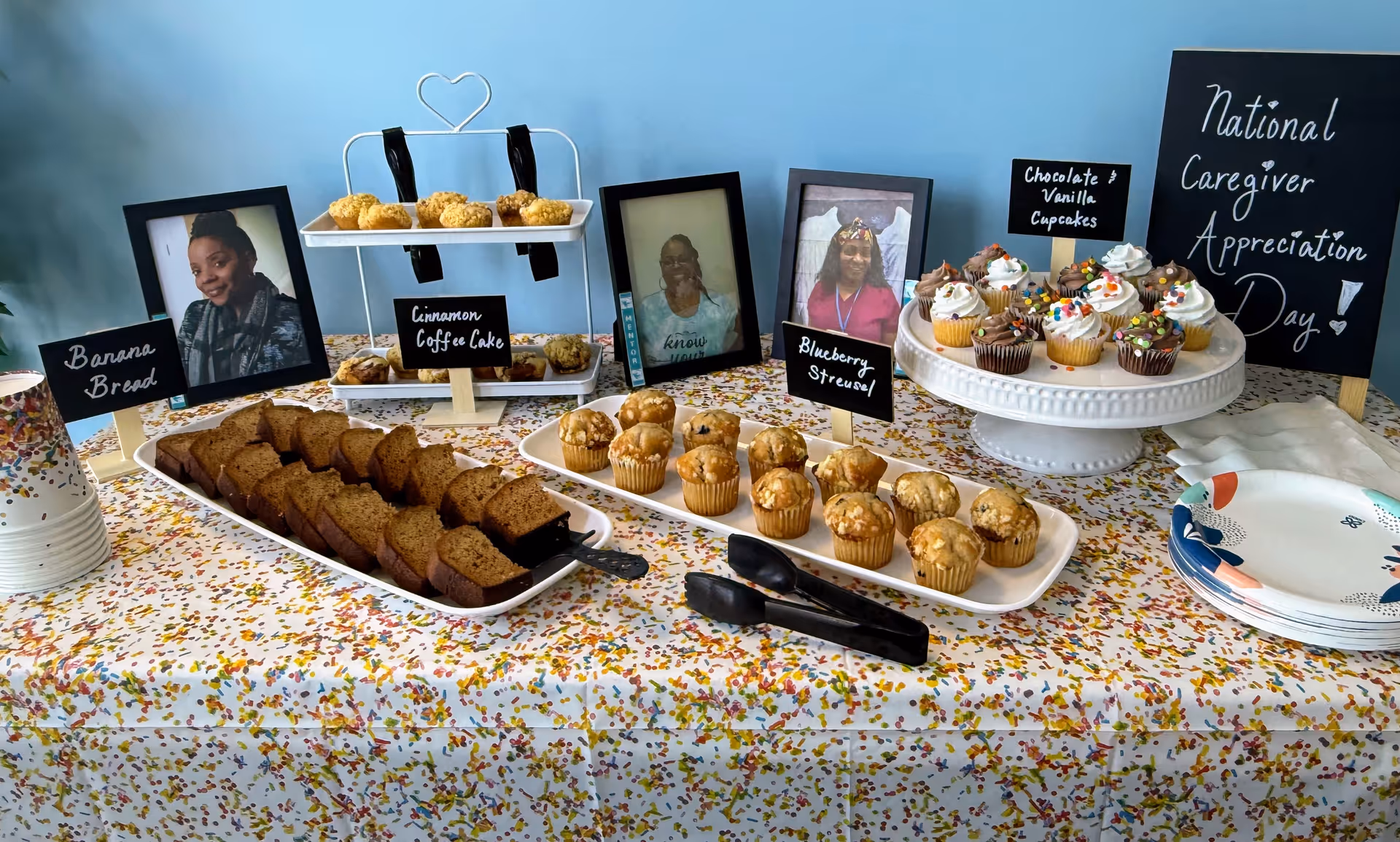 A dessert table with cupcakes, banana bread, photo frames, and appreciation signage.