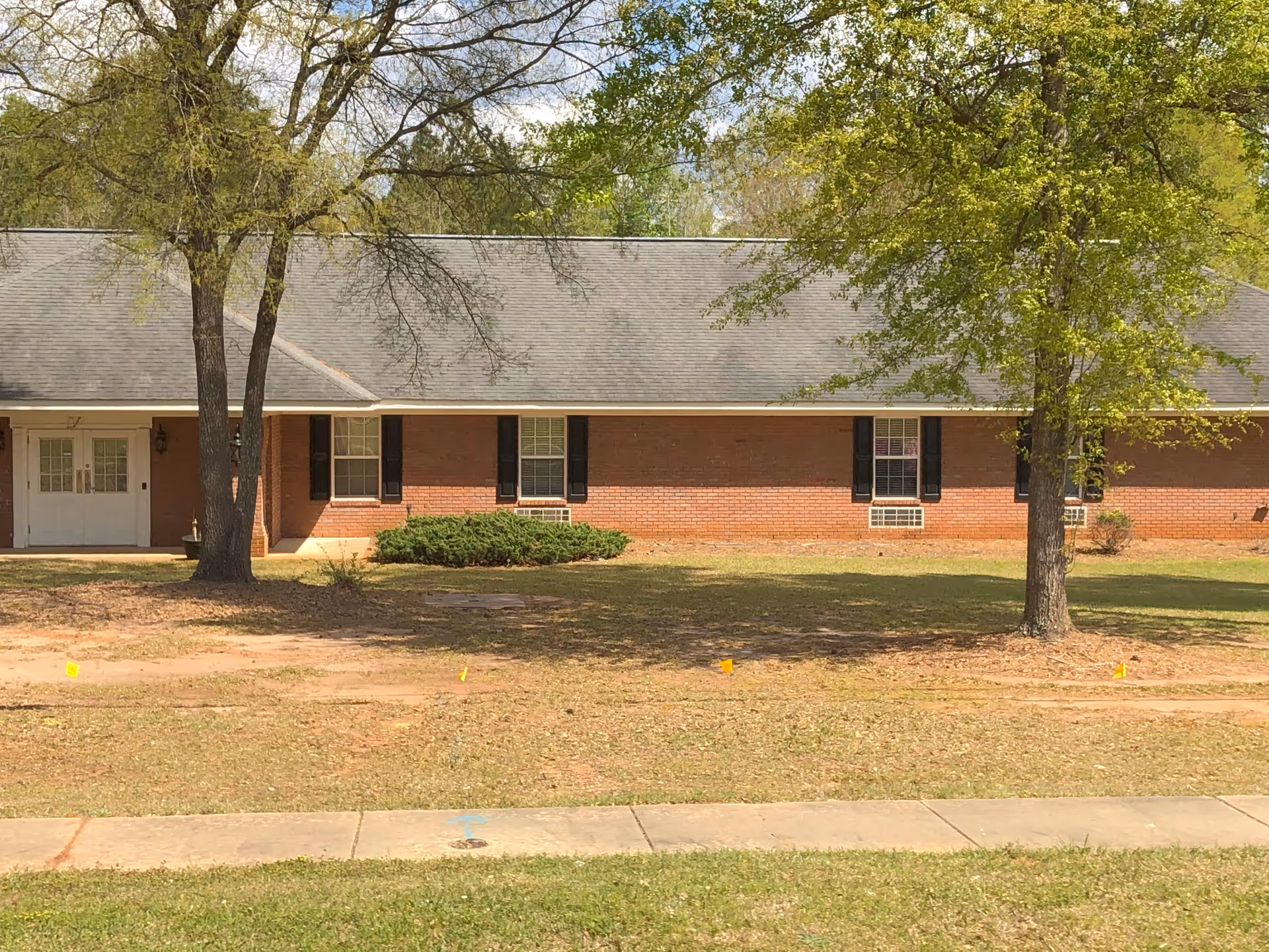 Brick single-story assisted living facility front with trees and a grassy lawn.