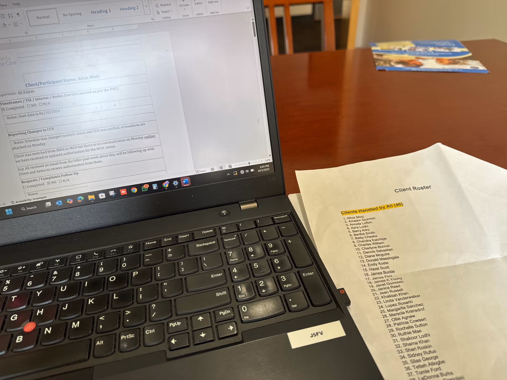 Laptop on a desk with a document visible on screen and a client roster sheet nearby.