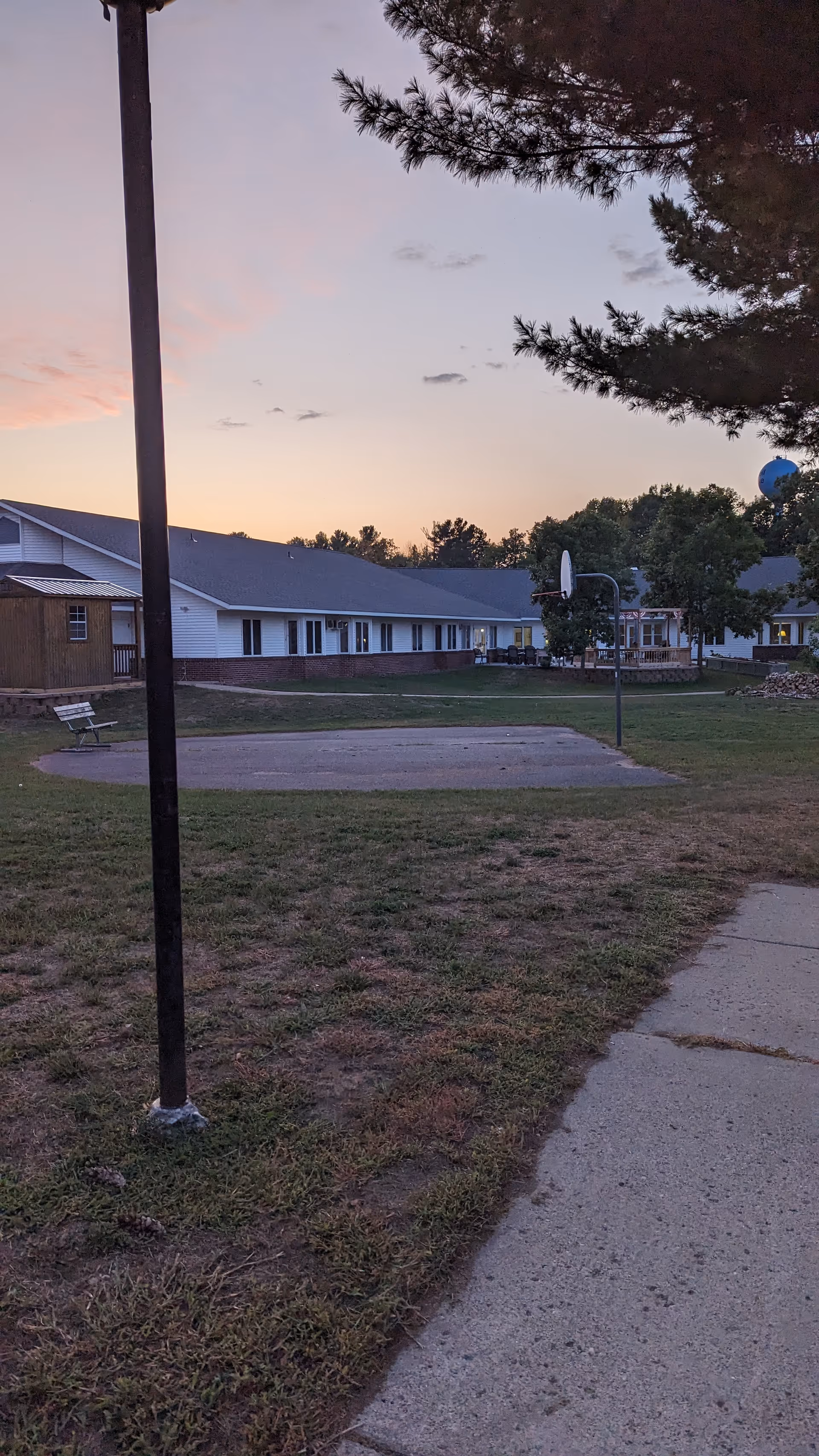 Sunset exterior of Glenview Special Care Wing with lawn, walkway, basketball hoop, and benches.