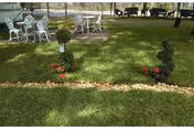 Outdoor lawn with white metal tables, chairs, and flower beds.