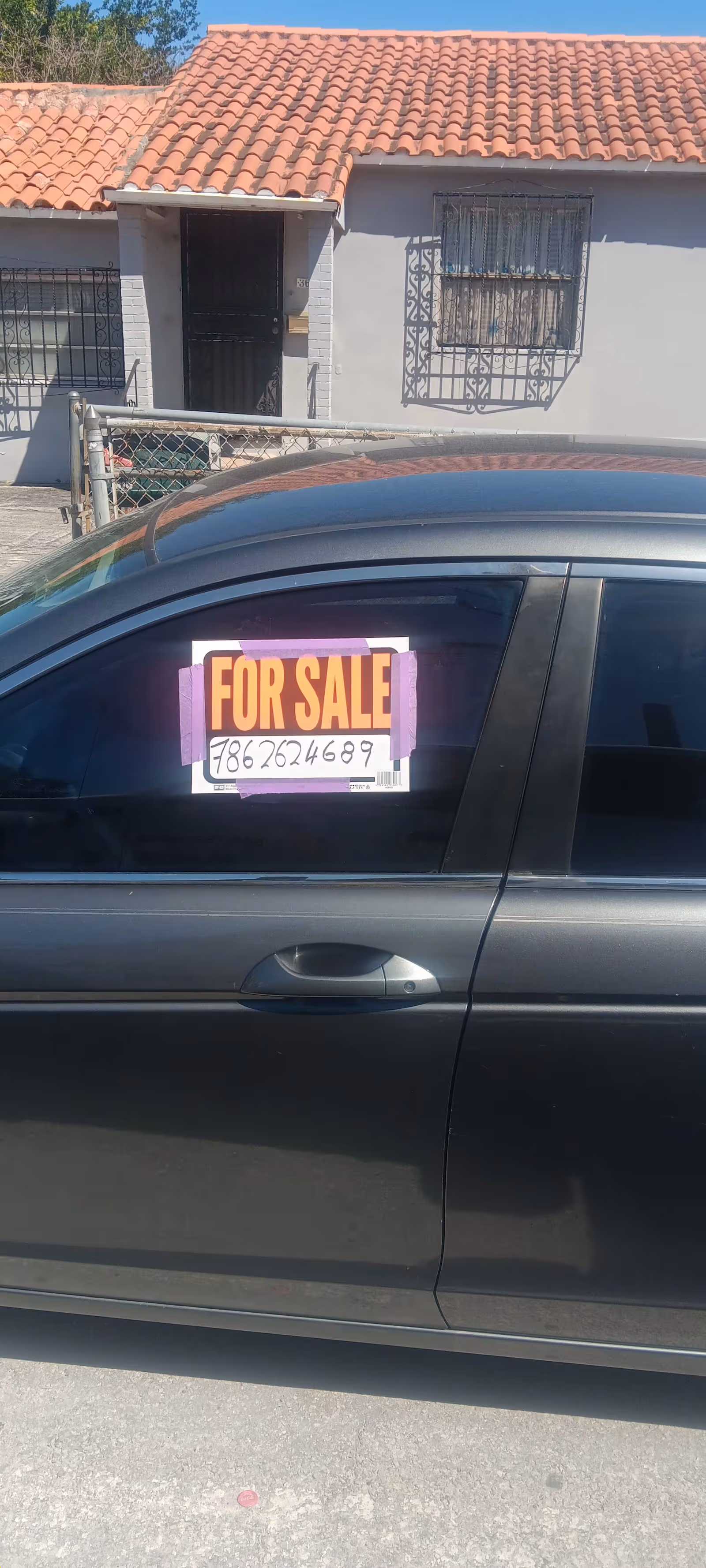 Front view of a house with a 'For Sale' sign on a car window.