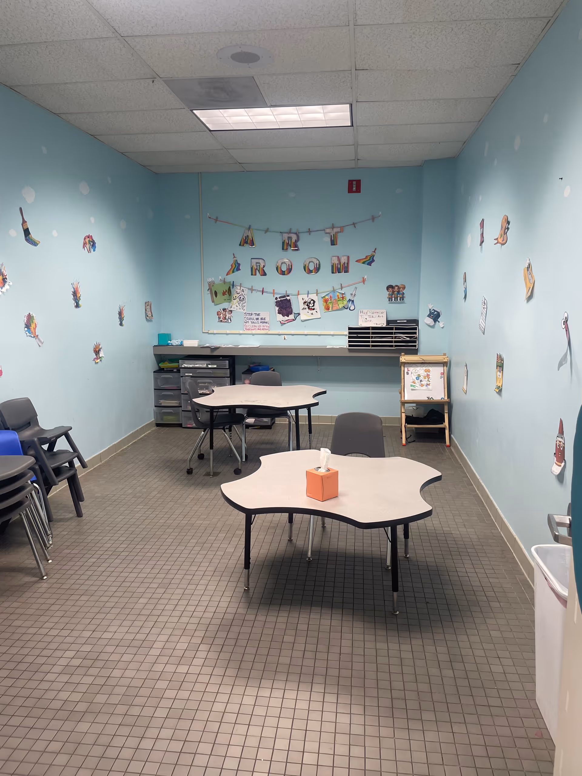 Bright blue art room with tables, chairs, and wall decorations.