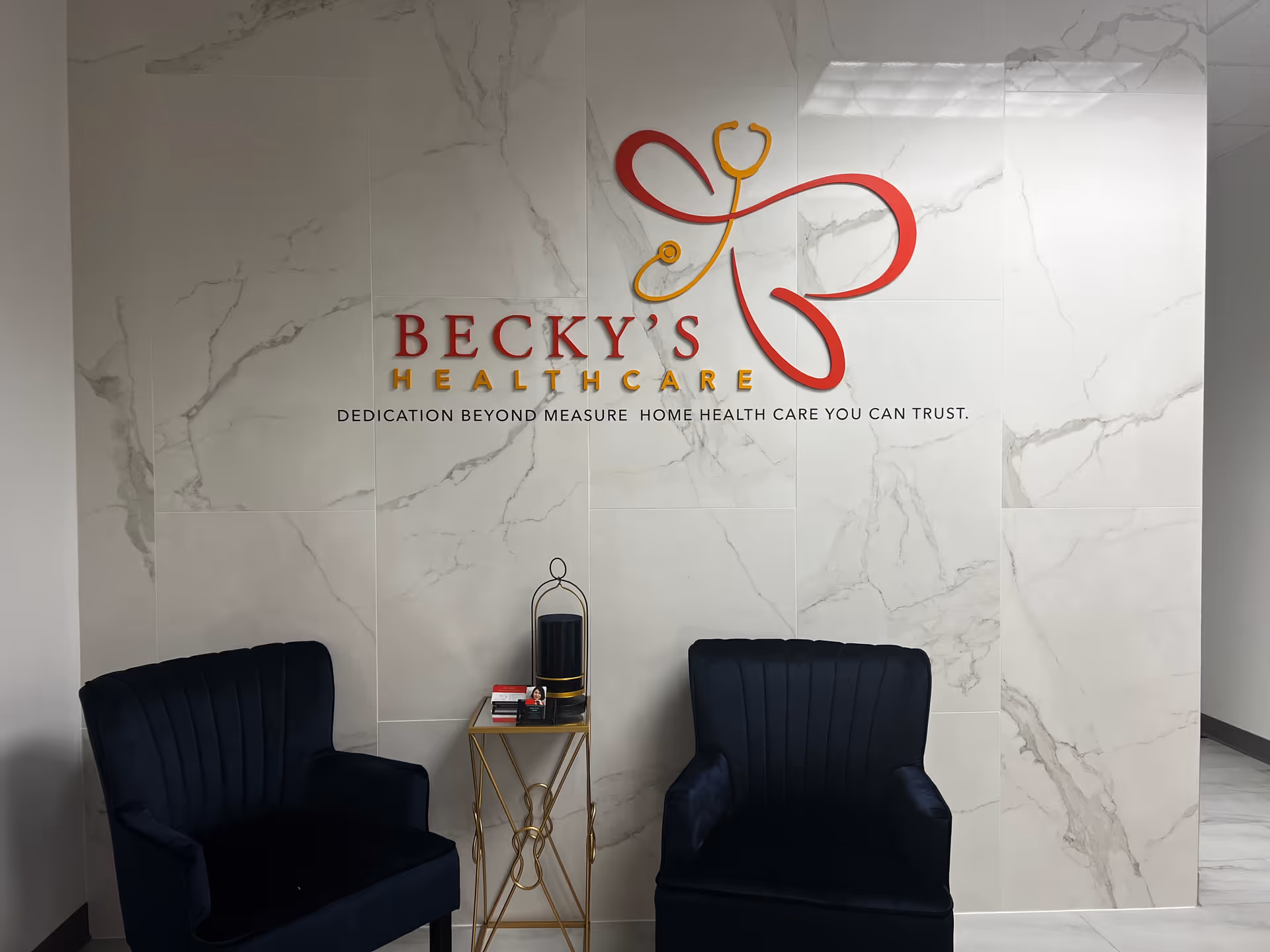 Marble-walled interior lobby with Becky's Healthcare logo, two dark blue chairs, and a small side table.