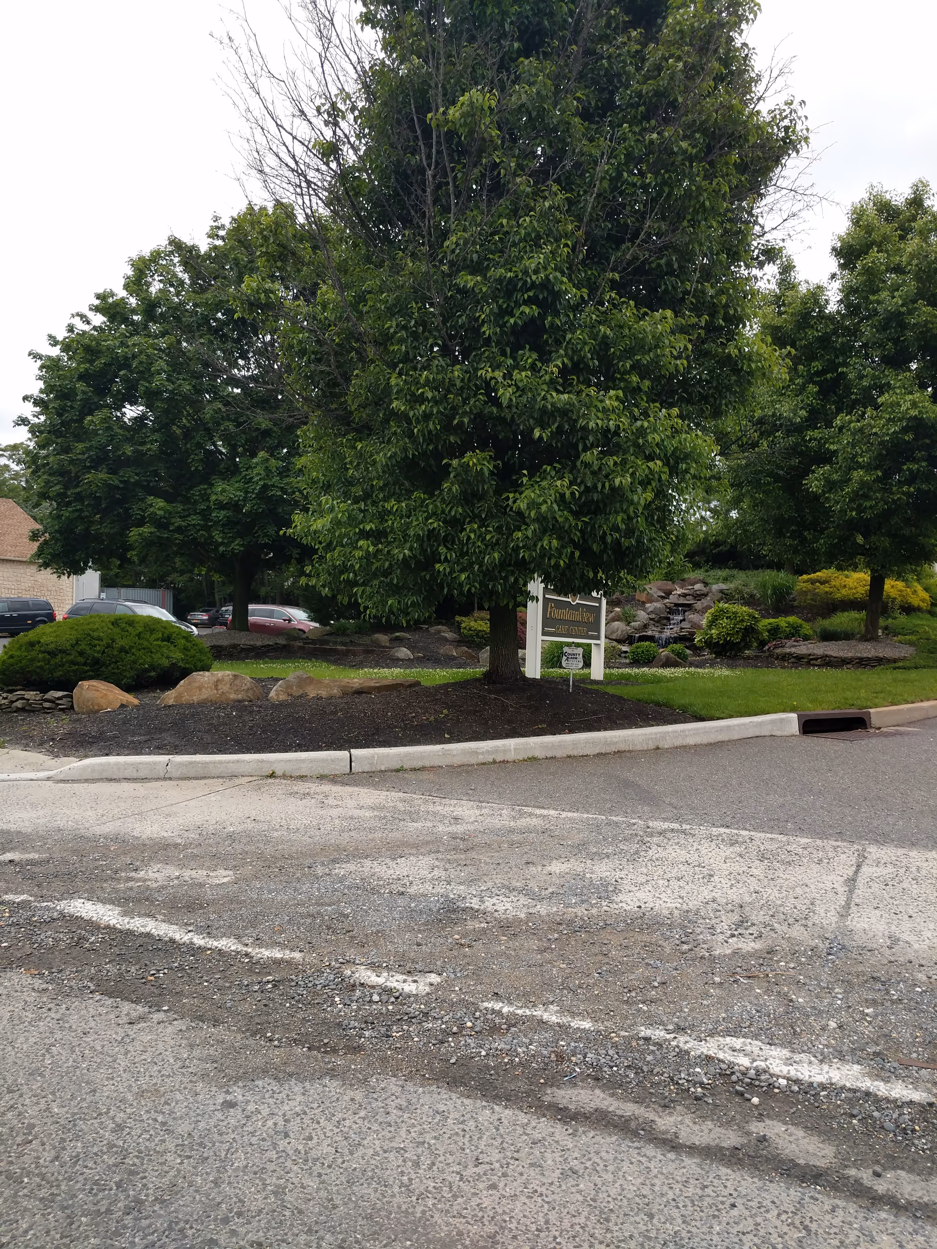 Parking lot in front of Fountain View Care Center with trees, landscaping, and a sign.
