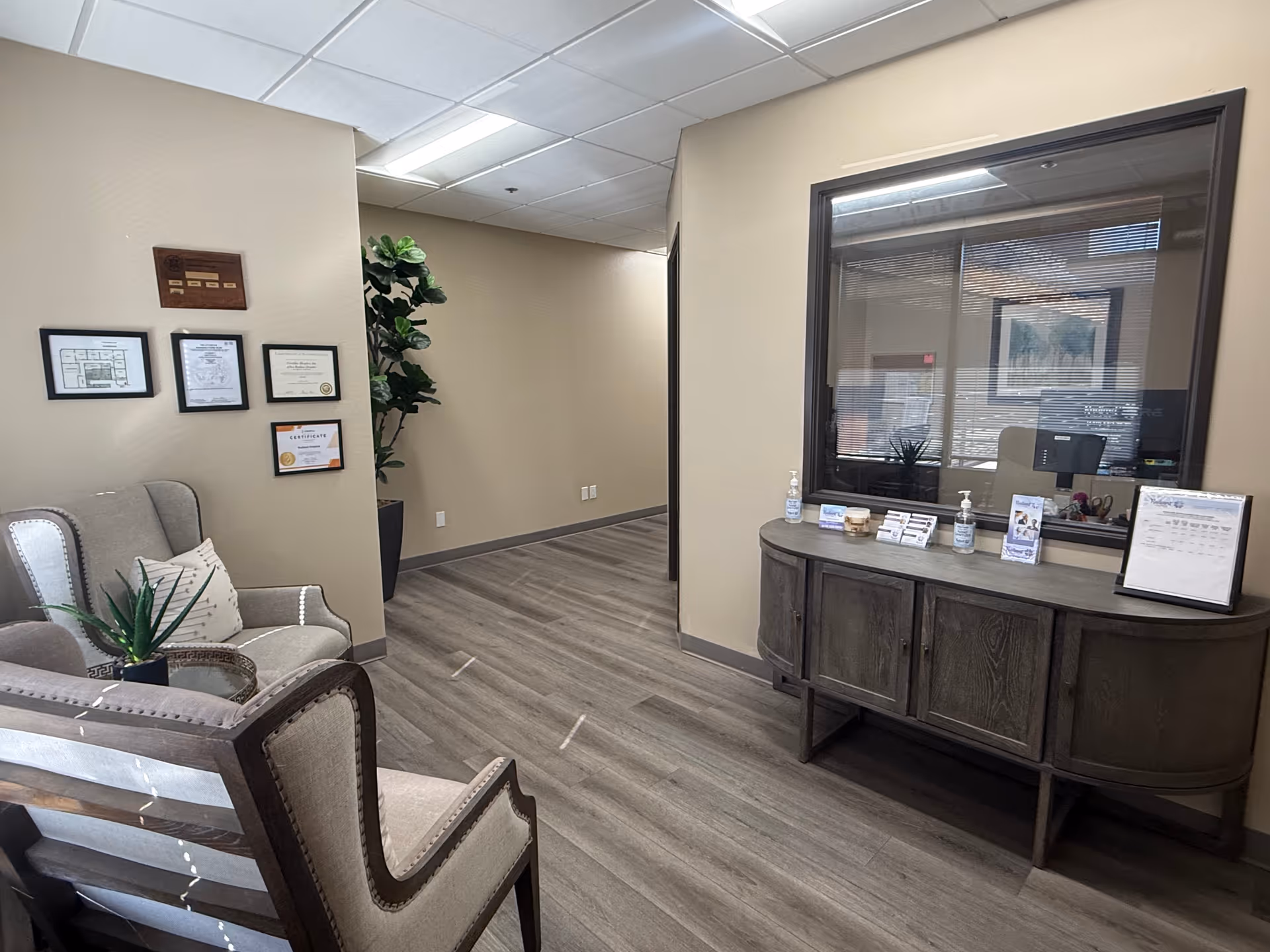 Reception lobby with a curved dark wood desk, beige walls, comfortable chairs, and plants.