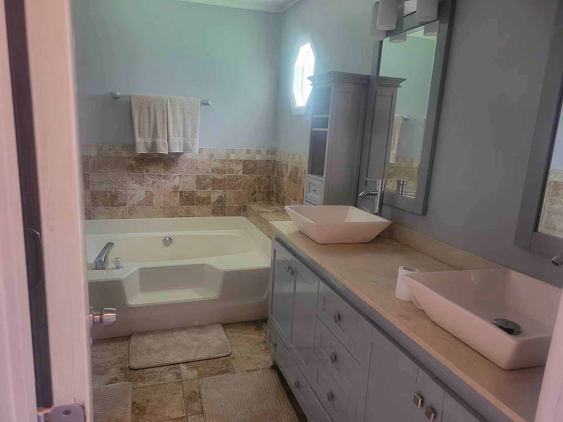 A bathroom with a bathtub, dual vessel sinks, and tiled walls.