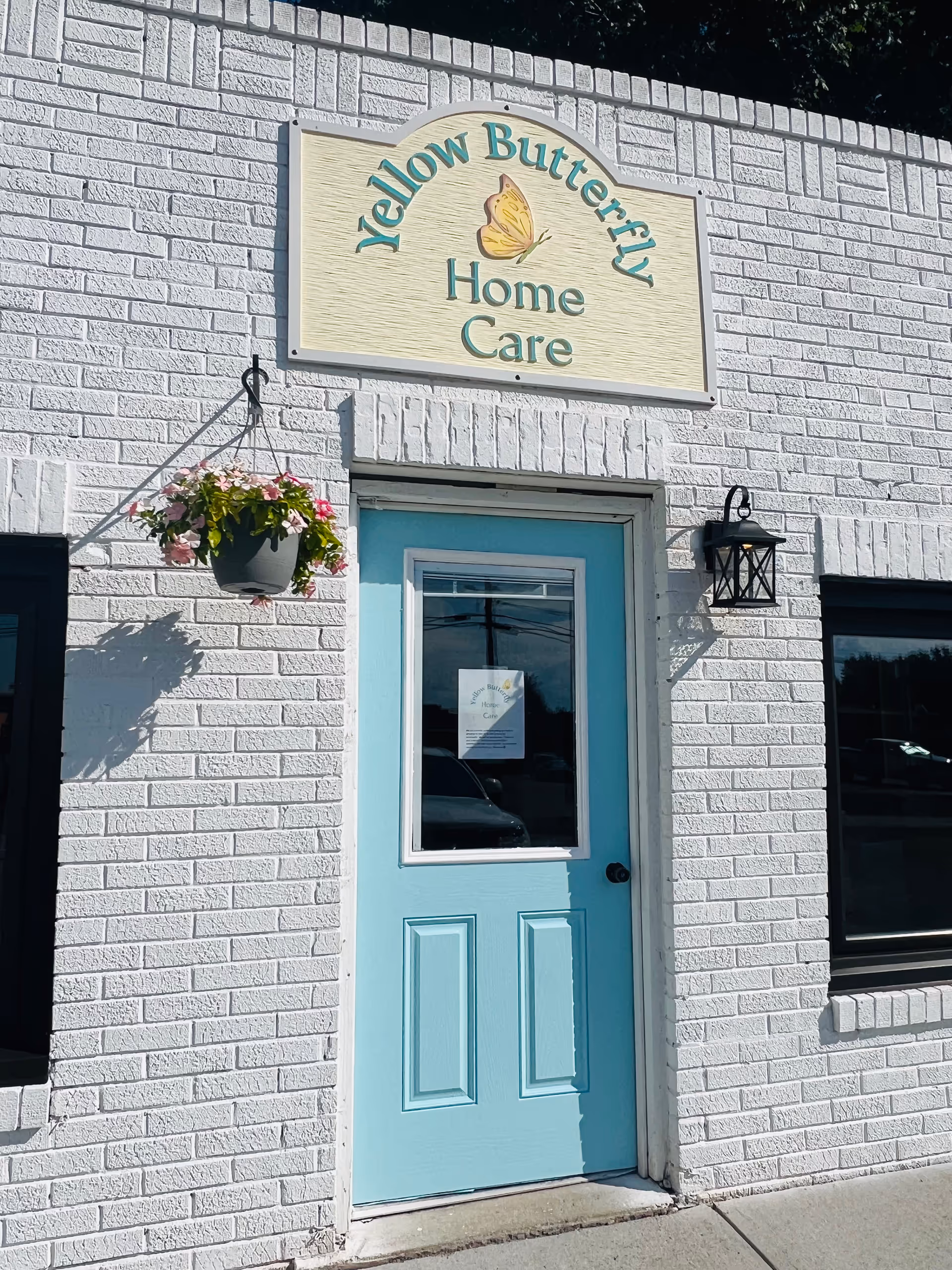 White brick building with a light blue door, hanging planter, and Yellow Butterfly Home Care sign.