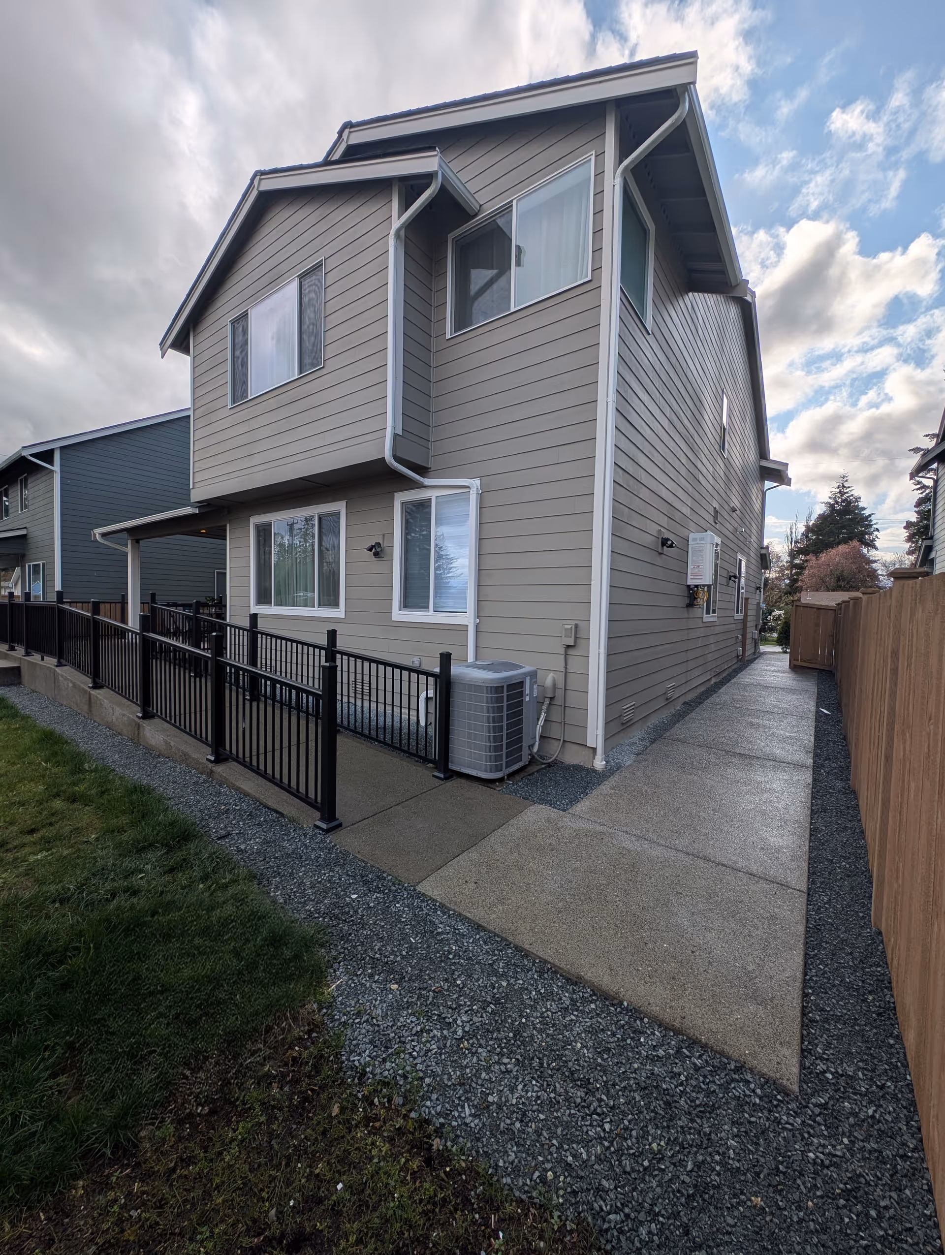 Two-story beige senior living home exterior with walkway, black railing, and outdoor utility unit