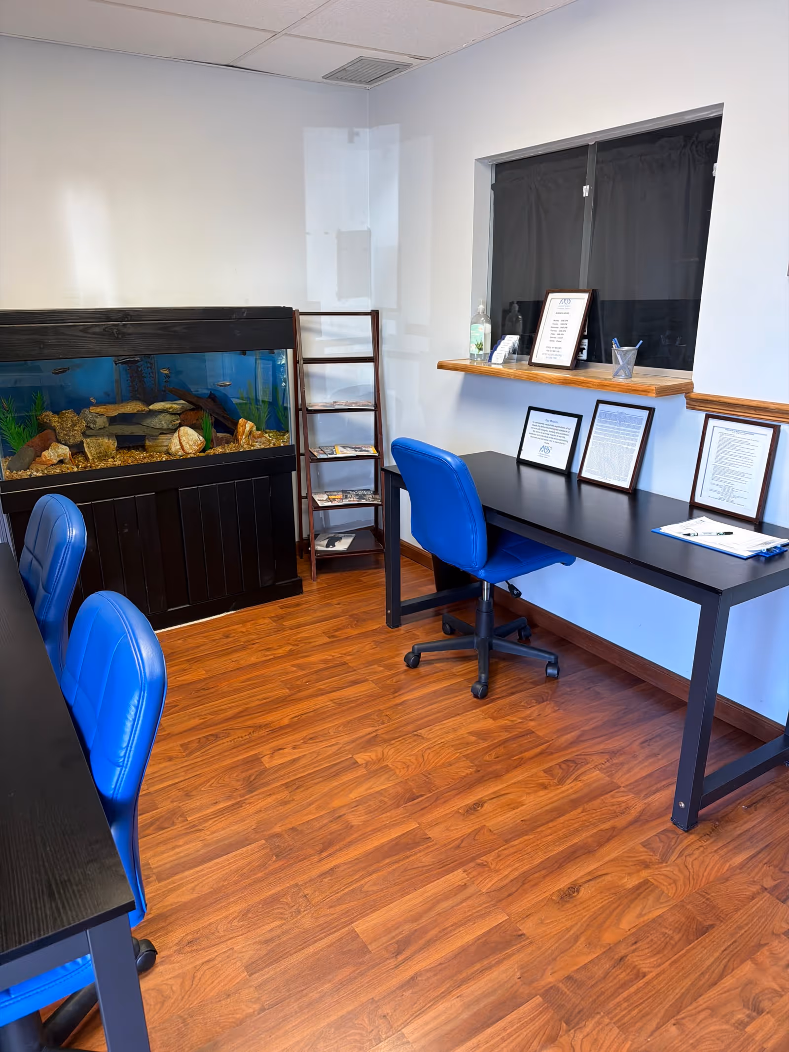 Office-like interior with blue chairs, black desks, an aquarium, and a window.