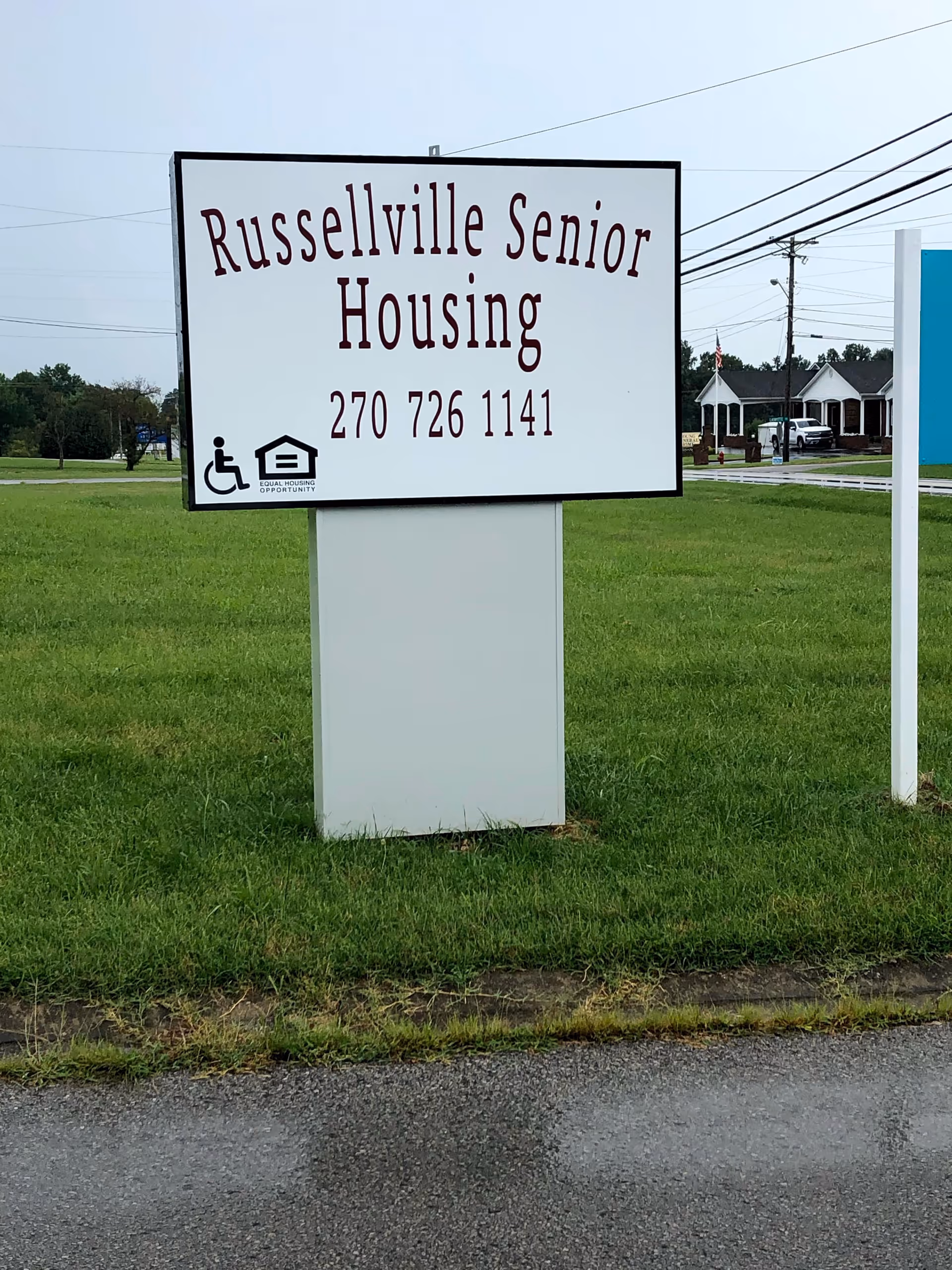 A large Russellville Senior Housing sign on a grassy lot with distant buildings visible.