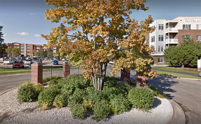 Exterior view of Knollwood Place Apartments showing a landscaped roundabout and building façade.