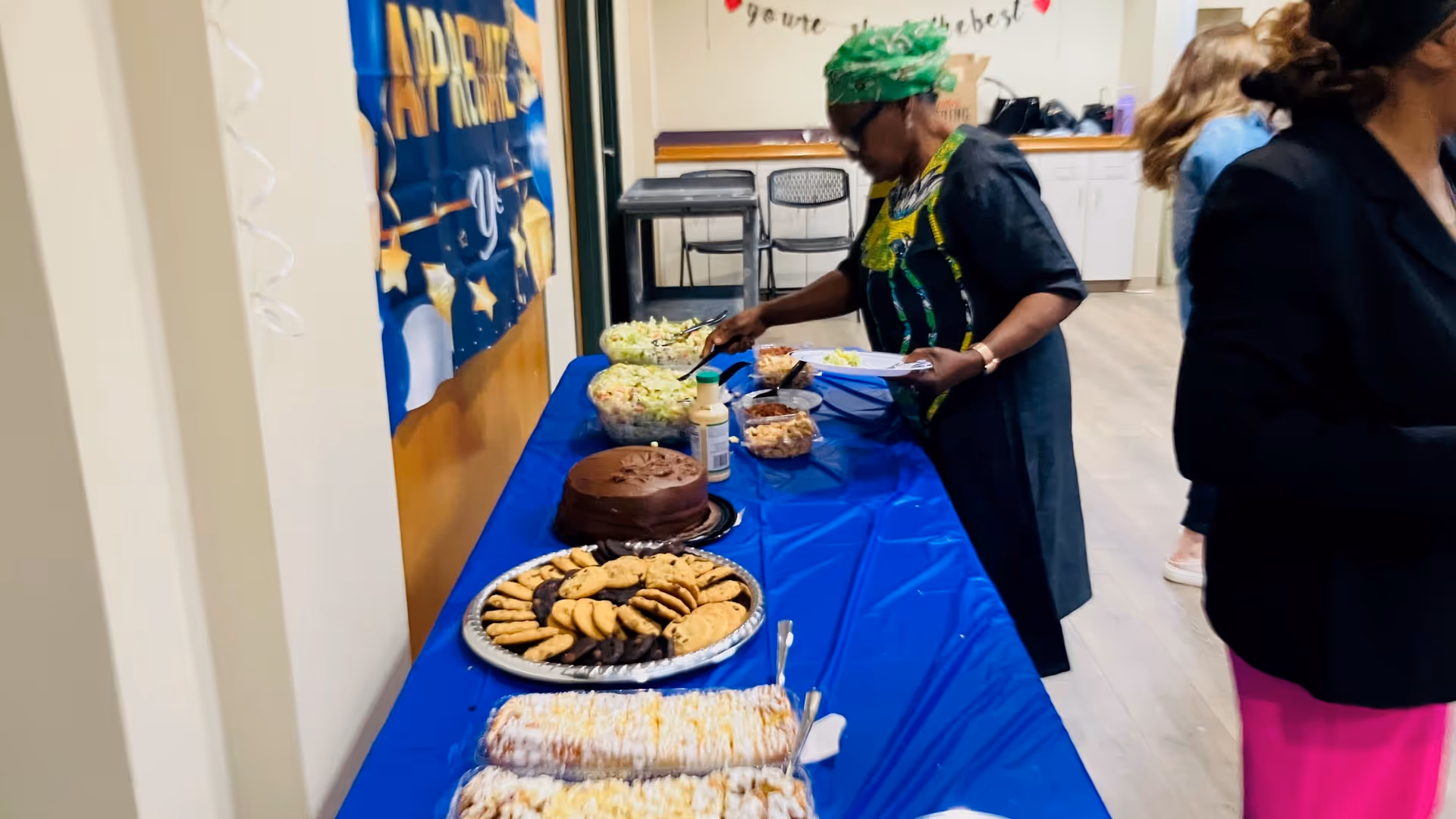 A staff member arranges desserts on a blue-covered dining table in a care facility.