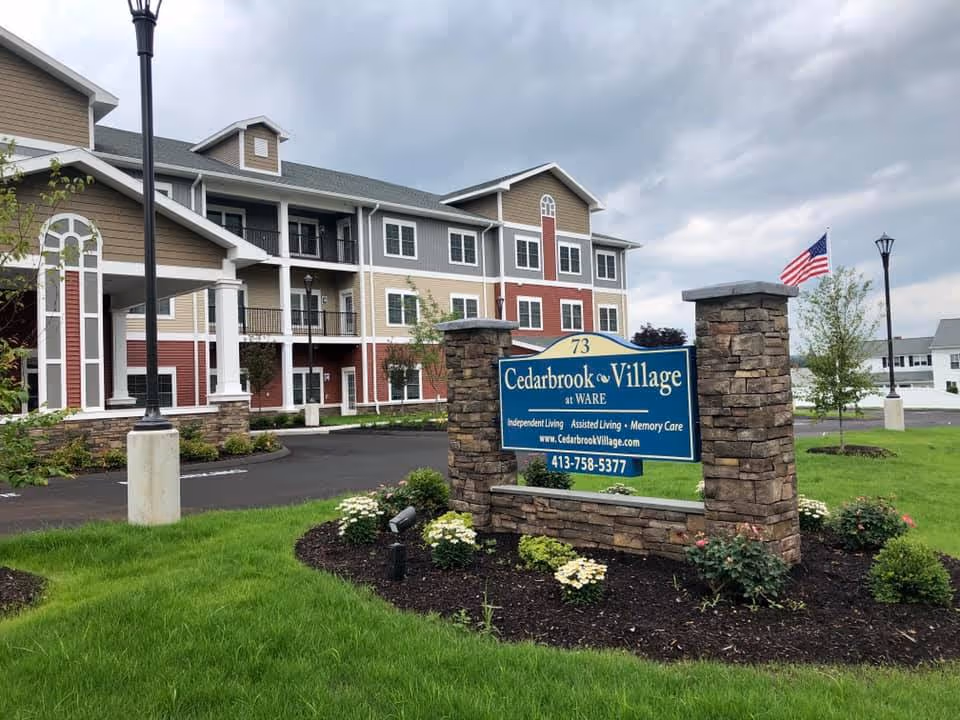 Exterior view of Cedarbrook Village senior living building with landscaped grounds and a blue sign.