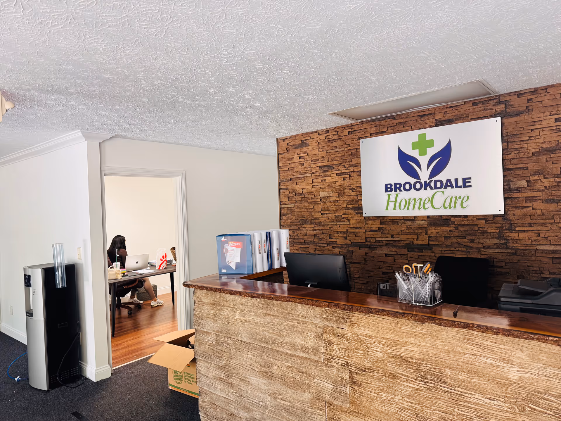 Reception area with Brookdale HomeCare sign, brick accent wall, and staff at desk.