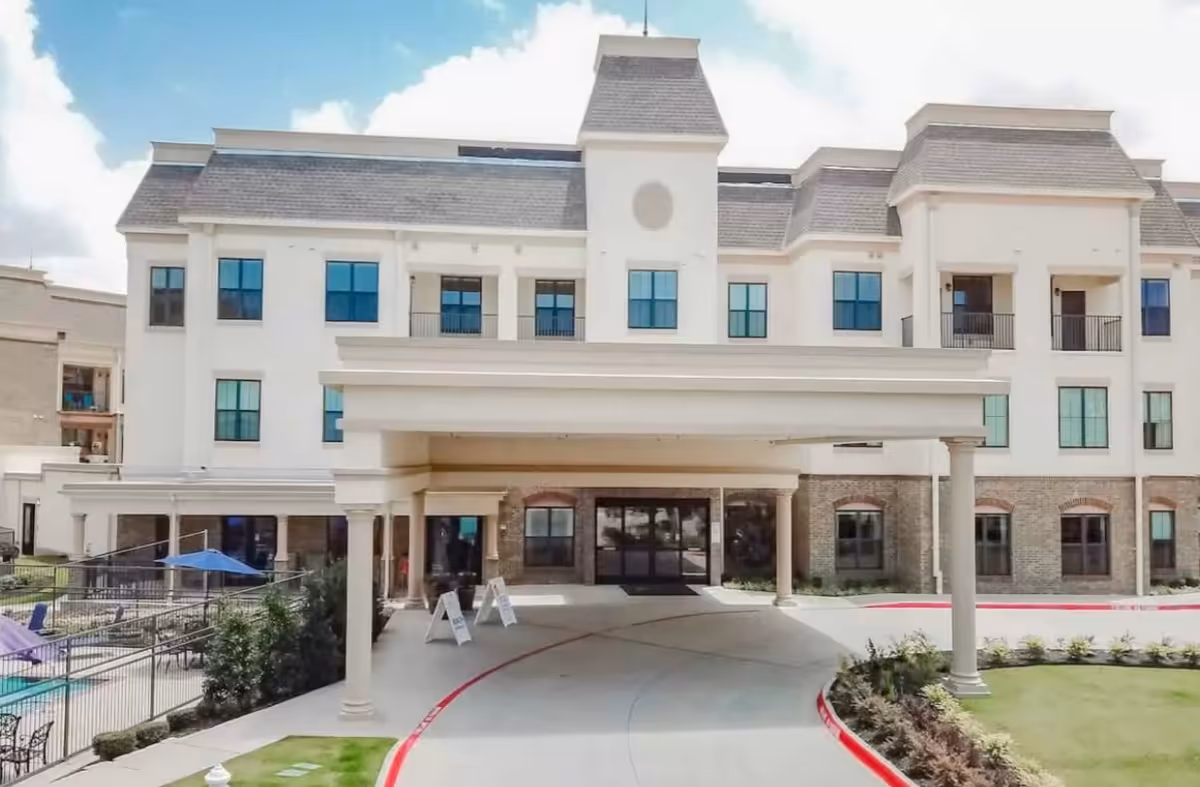 White multi-story senior living facility with a covered entrance and circular driveway.